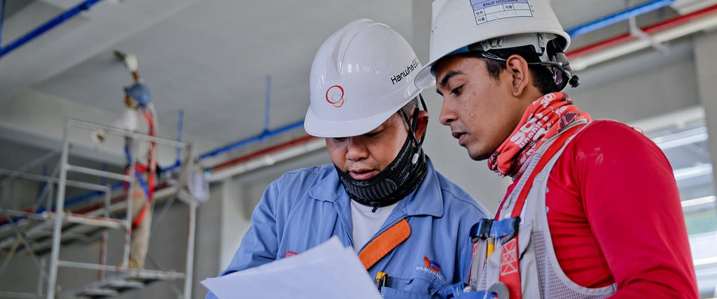 2 worker standing beside each other talking wearing safety helmets